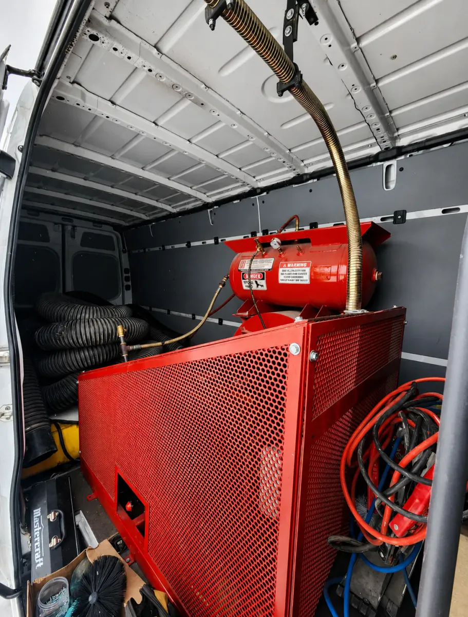 Truck-mounted air duct cleaning equipment and vacuum hoses inside a professional service van