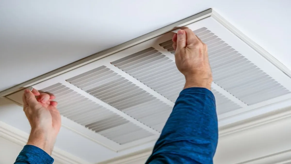 Technician removing a ceiling vent cover to clean the duct behind it